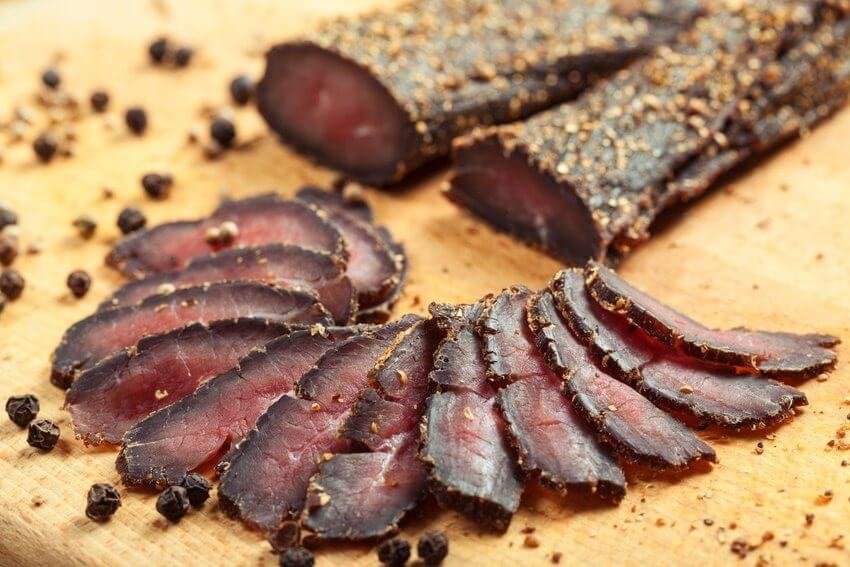 Thịt biltong Nam Phi thái lát trên thớt gỗ, rắc tiêu đen, tạo hương vị truyền thống đậm đà, hấp dẫn.