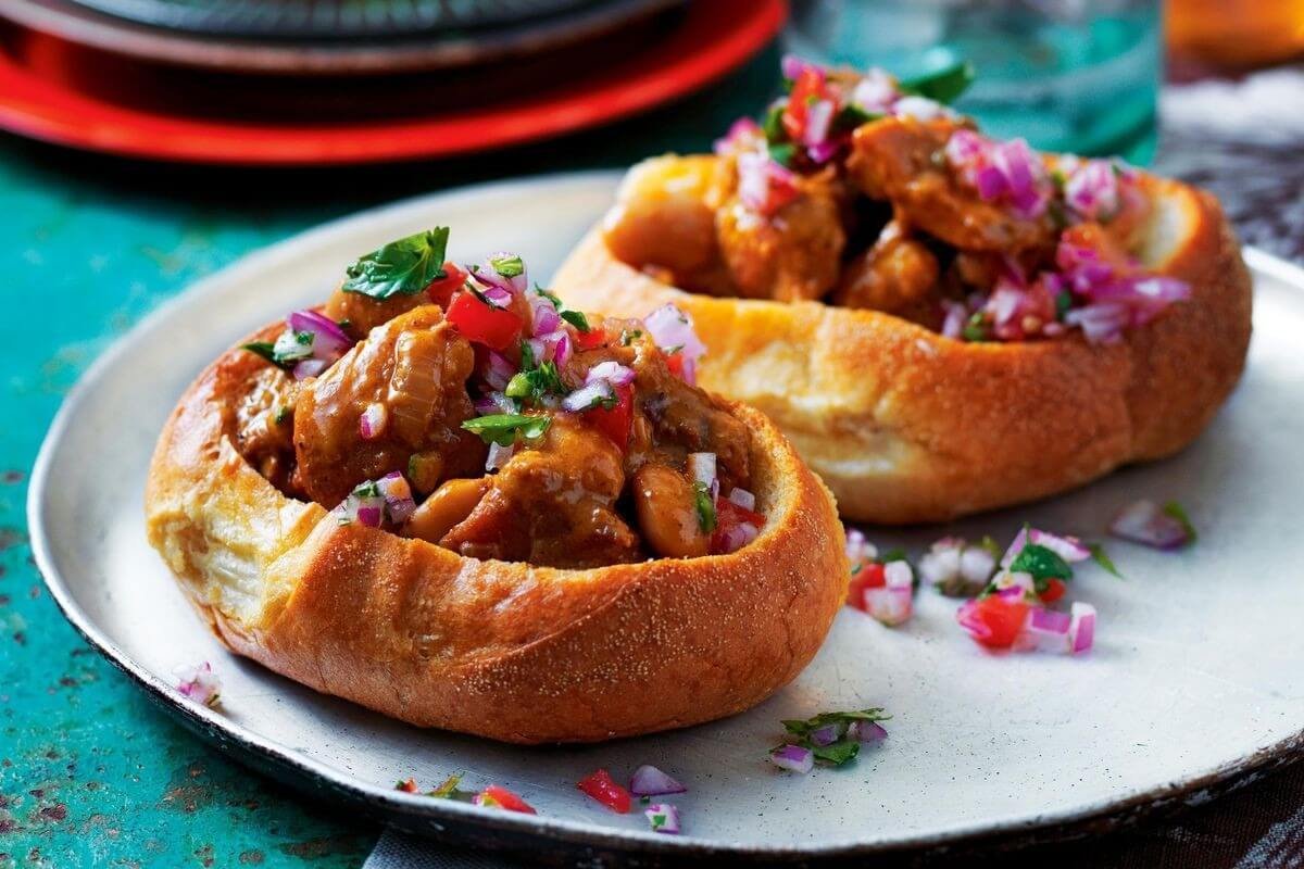 Bánh mì thuyền thơm ngon với nhân thịt cay, salad hành và rau sống, bày trí trên đĩa kim loại màu bạc sáng.