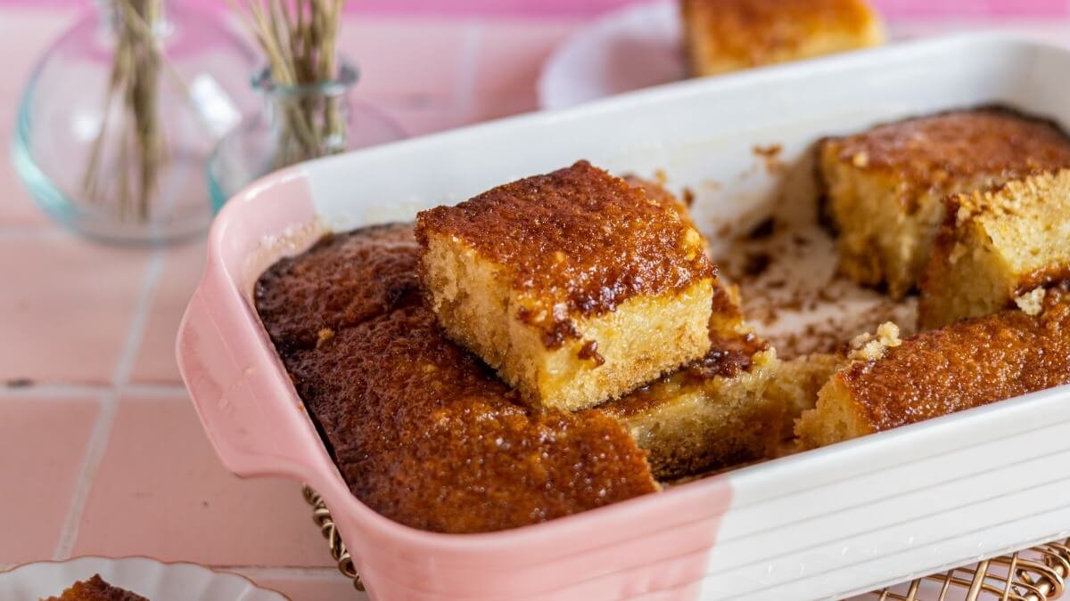 Bánh bông lan caramel tự làm trong khay nướng trắng, bánh nướng vàng giòn với lớp trên ngọt mịn, một lát được cắt ra.