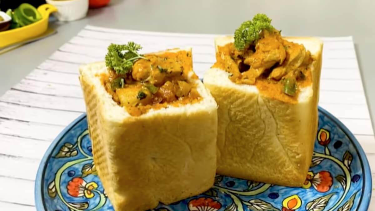 Hai khối bánh mì vuông được cắt lõi, nhồi thịt gà và rau củ sốt kem, trang trí rau mùi tươi lên trên.