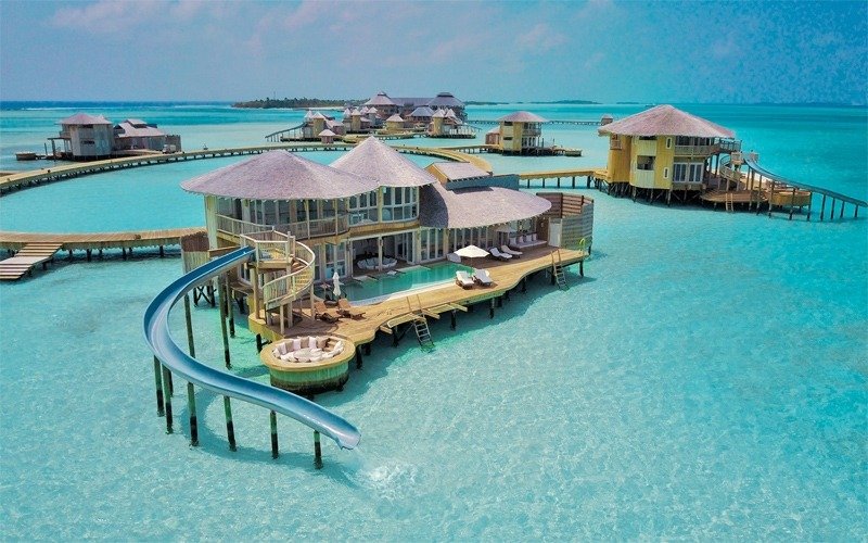 Khu nghỉ dưỡng sang trọng nằm trên nước xanh trong của Maldives, với nhà gỗ và cầu trượt ra biển.