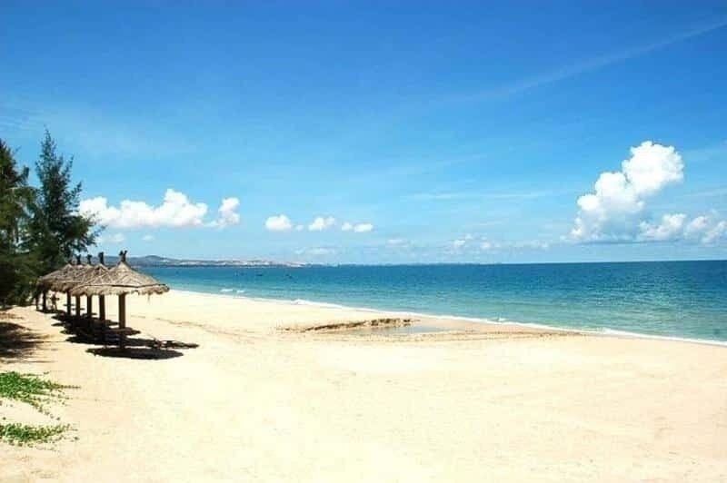 Bãi biển cát trắng mịn, nước biển xanh ngắt, bầu trời trong và hàng dù che mát dưới nắng hè.