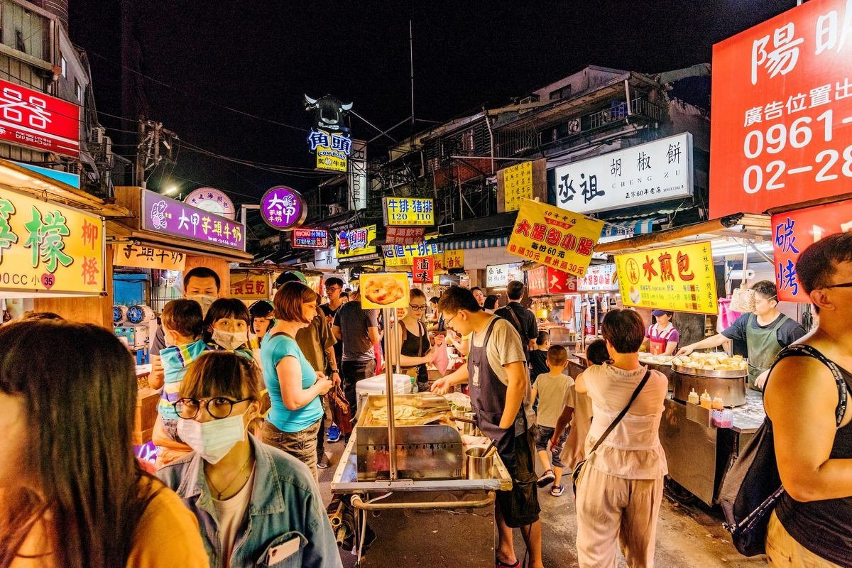 Chợ đêm Đài Loan với nhiều người mua sắm, thưởng thức món ăn đường phố dưới ánh sáng đèn neon rực rỡ.