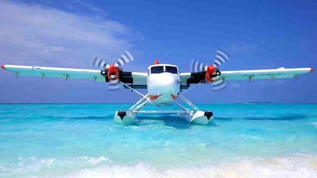 Thủy phi cơ đậu trên mặt nước biển xanh trong vắt, cánh quạt quay, bầu trời xanh không mây phía xa.