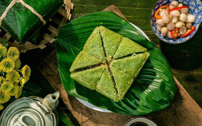 Bánh chưng xanh cắt miếng trên lá chuối, cùng bình trà cổ và đĩa dưa hành muối đặc trưng ngày Tết Việt Nam.