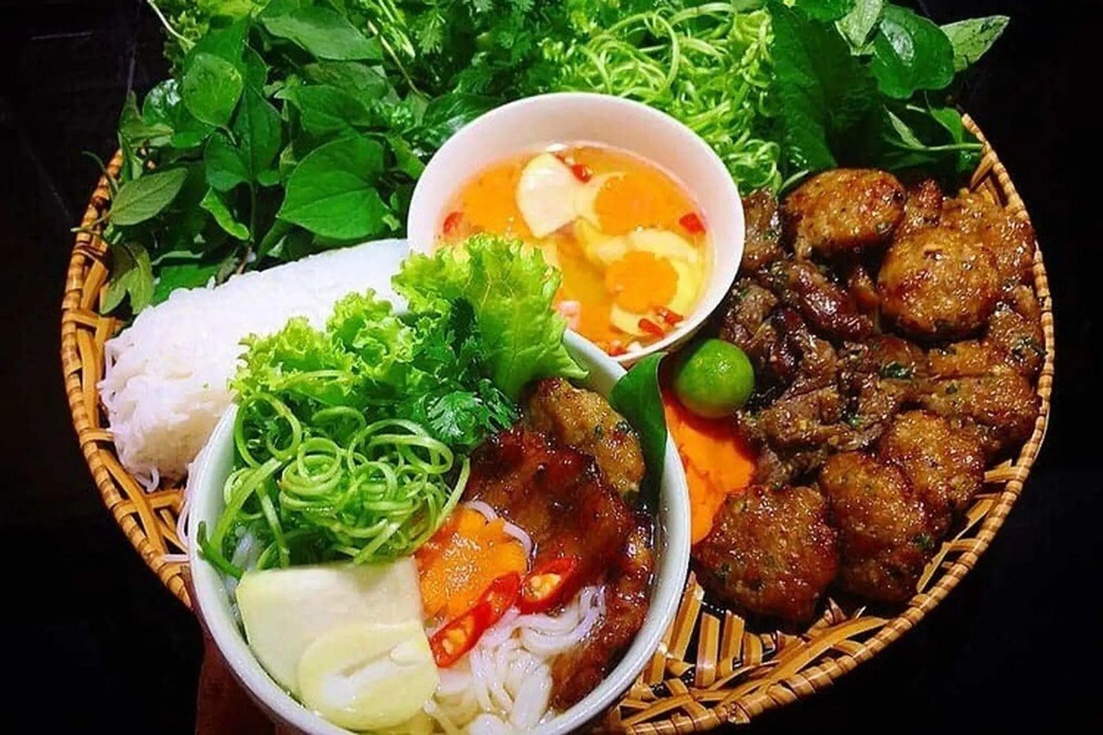 Đĩa bún chả Việt Nam gồm bún, chả nướng, rau sống và nước mắm chua ngọt hấp dẫn trên nền đan tre.