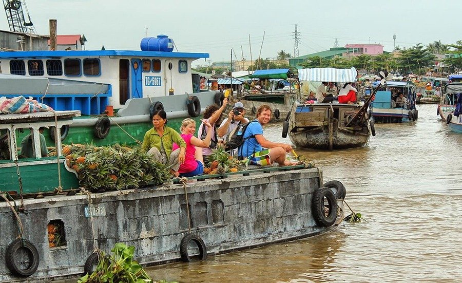 Thuyền bán hàng trên chợ nổi đông đúc, du khách tận hưởng và chụp ảnh, thể hiện văn hóa sông nước Việt Nam.