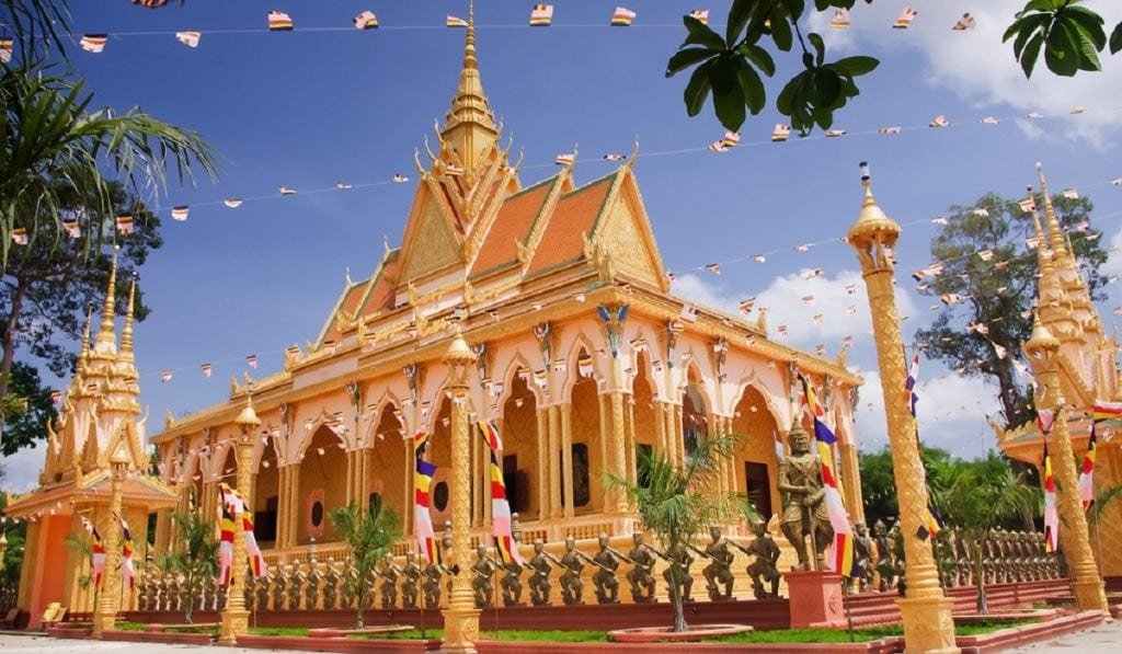 Ngôi chùa Phật giáo lớn với kiến trúc truyền thống, mái vàng rực rỡ, cờ bay, cây xanh xung quanh, trời xanh.