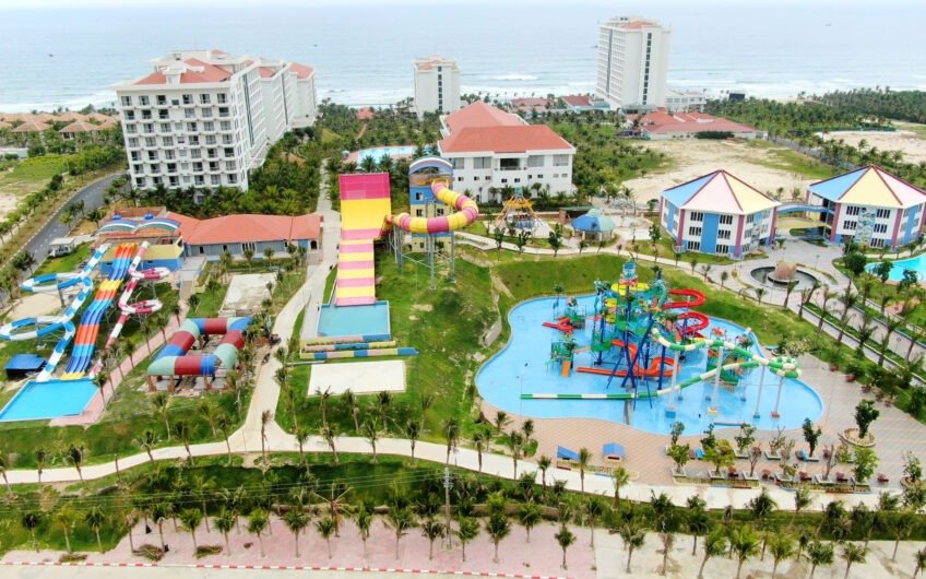 Khu vực công viên nước với các toà nhà cao tầng gần biển, bao gồm cầu trượt nước và hồ bơi sặc sỡ.