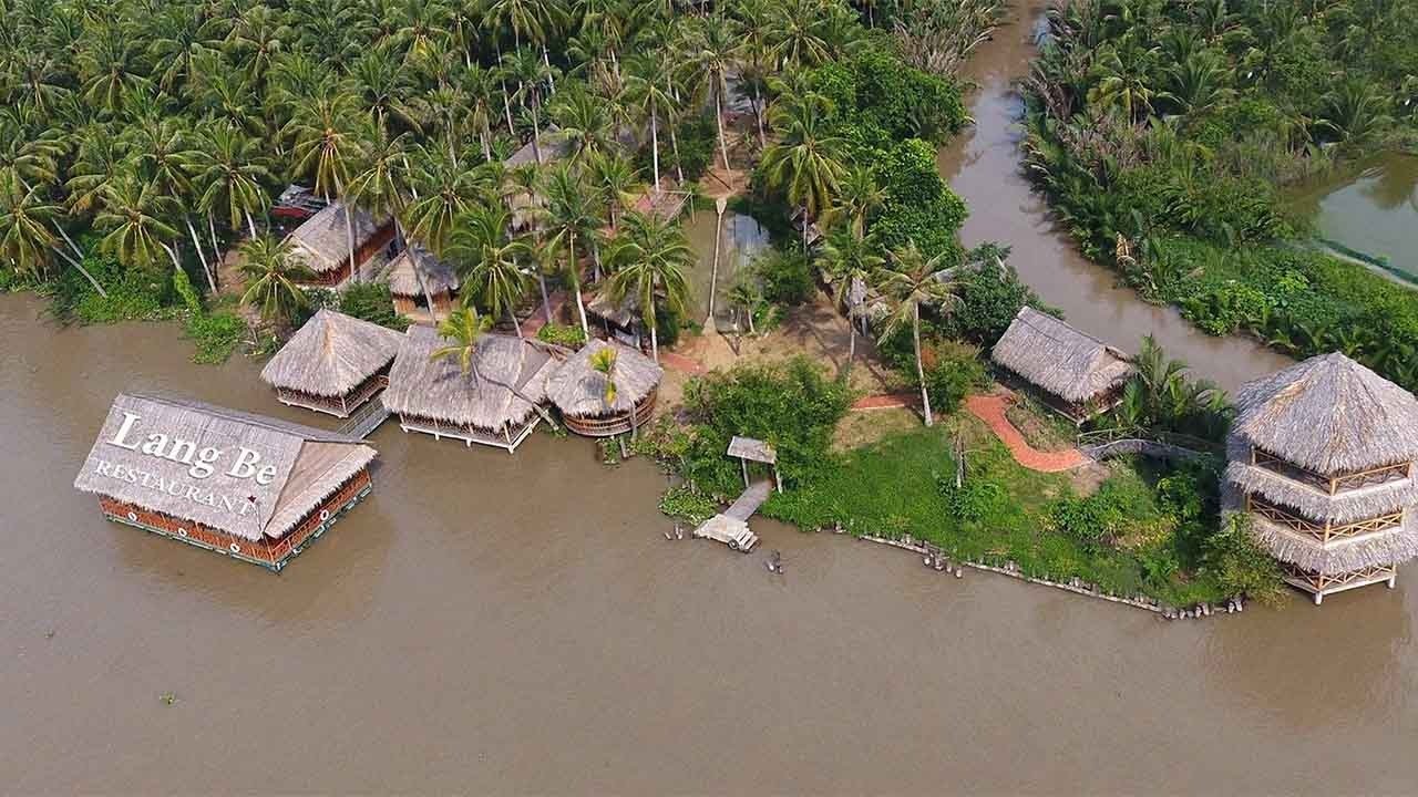 Nhà hàng Làng Bè bên bờ sông xanh, nổi bật với mái tranh giữa rừng cây dừa, tạo cảm giác miền quê yên bình.