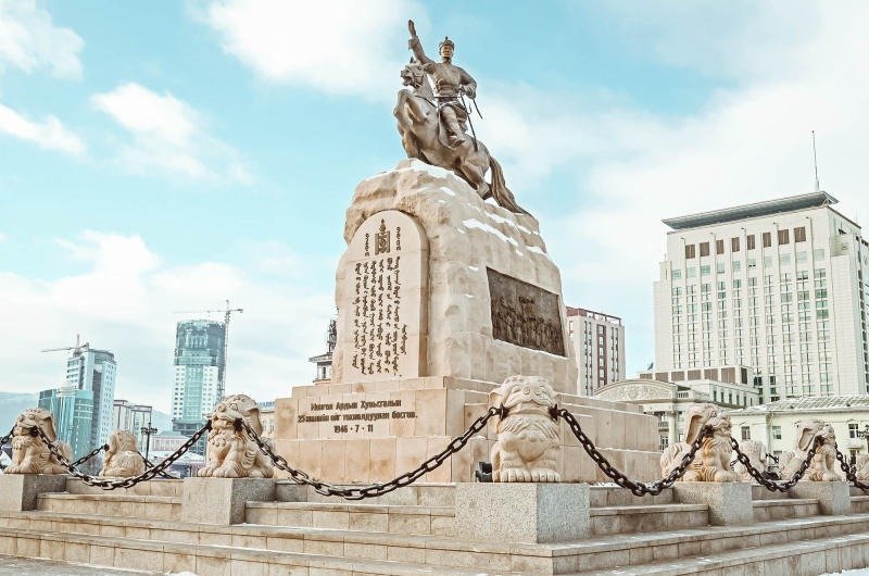 Tượng đài uy nghi với binh lính cưỡi ngựa, nền trời xanh và toà nhà hiện đại phía sau tại trung tâm thành phố.