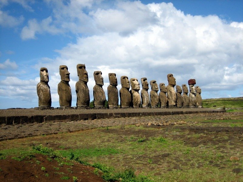 Dãy tượng Moai trên đảo Phục Sinh dưới bầu trời xanh có mây trắng, bãi cỏ xanh và nền đất đá.