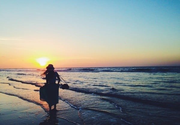 Người đi bộ trên bãi biển lúc hoàng hôn, với ánh mặt trời vàng cam lung linh trên mặt nước.