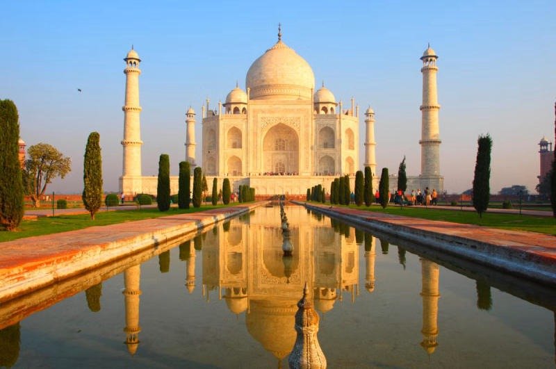 Lăng Taj Mahal trắng muốt phản chiếu trên mặt nước trong xanh dưới ánh nắng ban mai rực rỡ.