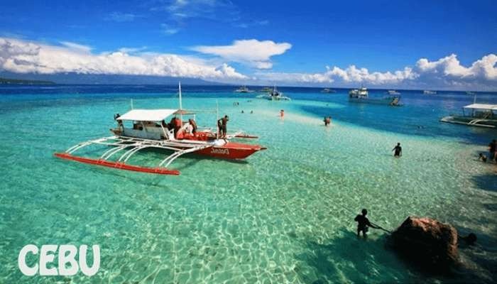 Khung cảnh bãi biển Cebu tuyệt đẹp với sắc xanh ngọc, thuyền gỗ truyền thống và du khách vui chơi dưới ánh nắng.