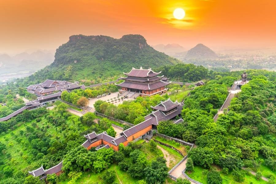 Ngôi chùa trên núi xanh, giữa rừng cây, với mặt trời lặn buổi hoàng hôn và phong cảnh hùng vĩ.