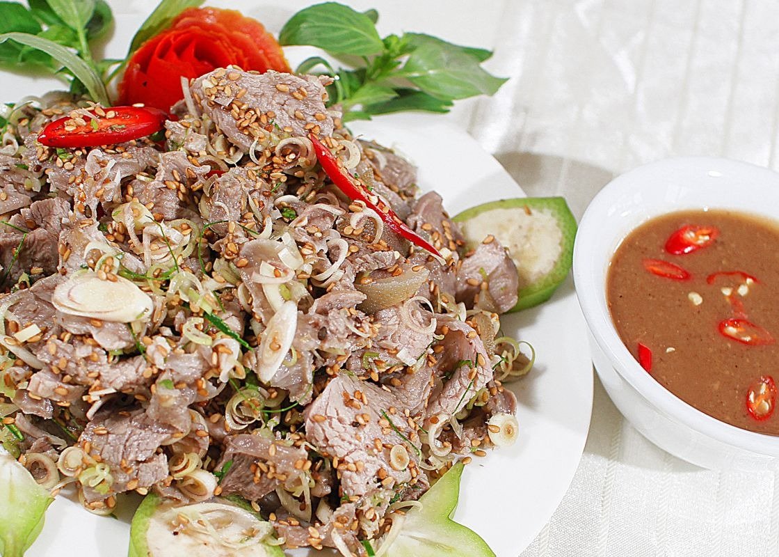 Gỏi bò bóp thấu với sả và mè rang, trang trí cùng ớt tươi, kèm chén mắm nêm đậm đà, hấp dẫn trên nền trắng.
