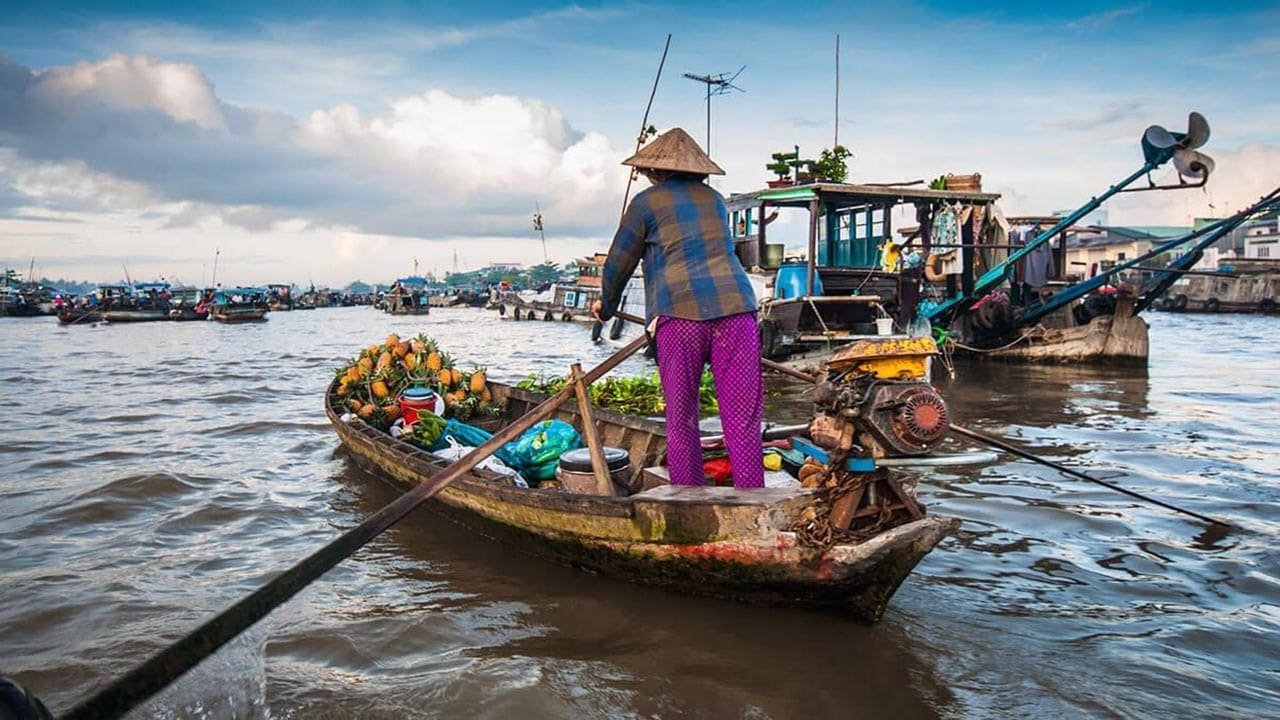 Người phụ nữ trên thuyền buôn bán trái cây tại chợ nổi trên sông, khung cảnh đặc trưng của miền sông nước.