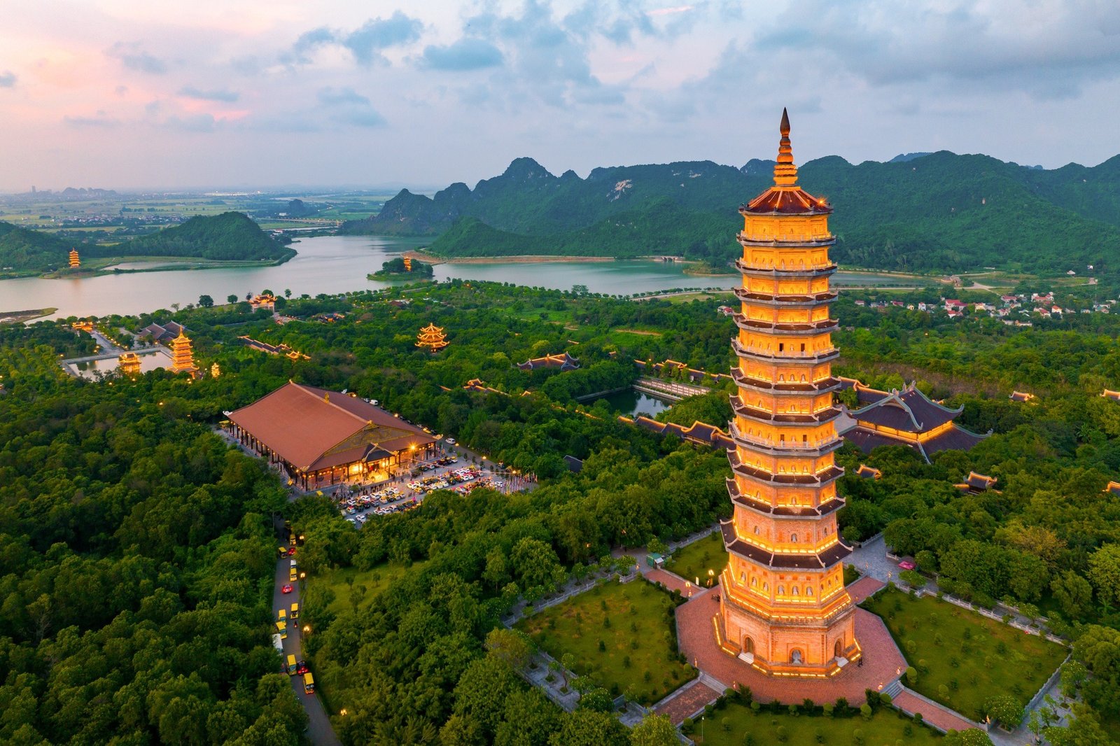 Chùa Bái Đính nhìn từ trên cao, với tháp cao nổi bật giữa rừng xanh và núi non hùng vĩ trong hoàng hôn.
