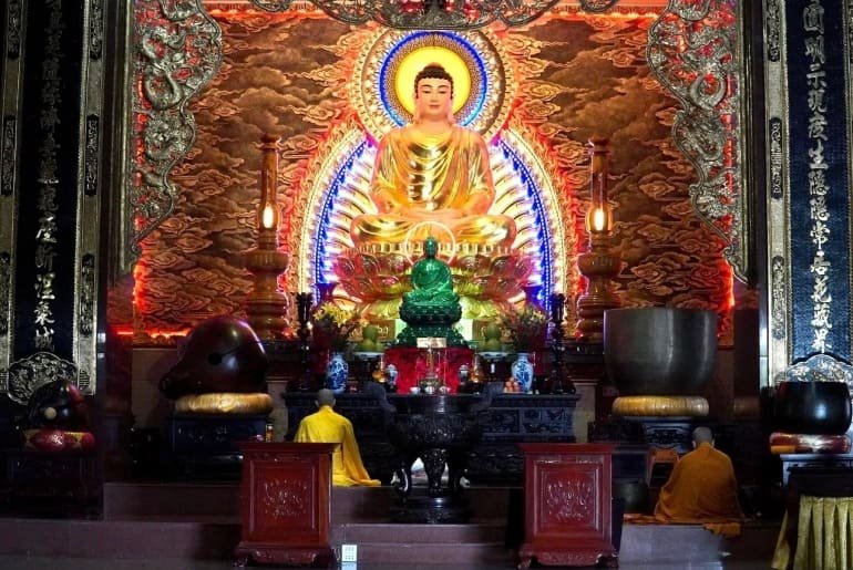 Tượng Phật lớn trong chùa, ánh đèn lung linh và người tu hành cầu nguyện trước bàn thờ trang nghiêm.