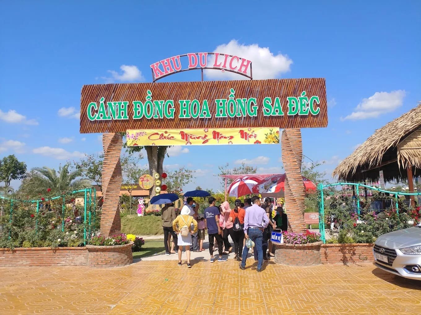 Du khách đang tham quan Khu du lịch Cánh Đồng Hoa Hồng Sa Đéc với cổng chào nổi bật dưới bầu trời trong xanh.
